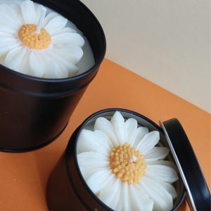 Vela artesana de soja ecologica con aroma floral y forma de margarita. En una lata metálica negra con tapa.